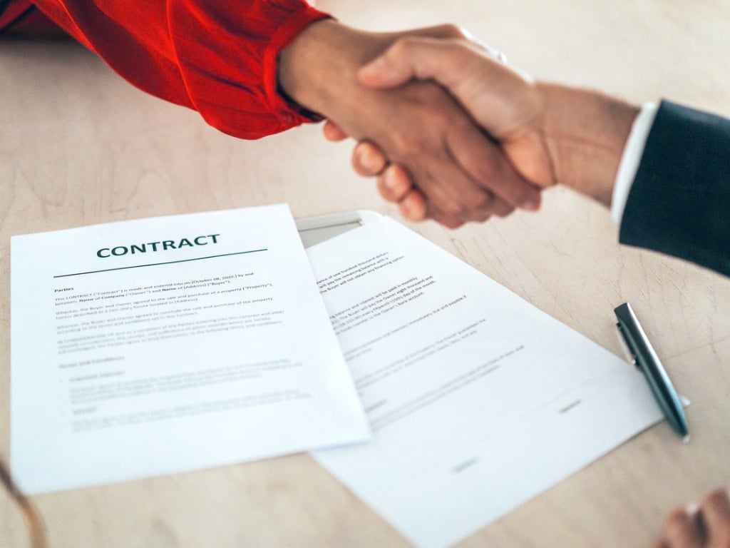 Two people shake hands over a contract, symbolizing a business agreement or deal closing.