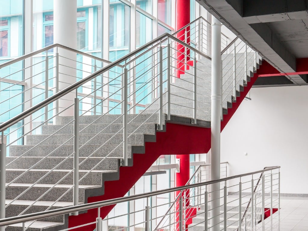 Modern interior staircase with granite steps and red accents, stainless steel railings, and large windows.