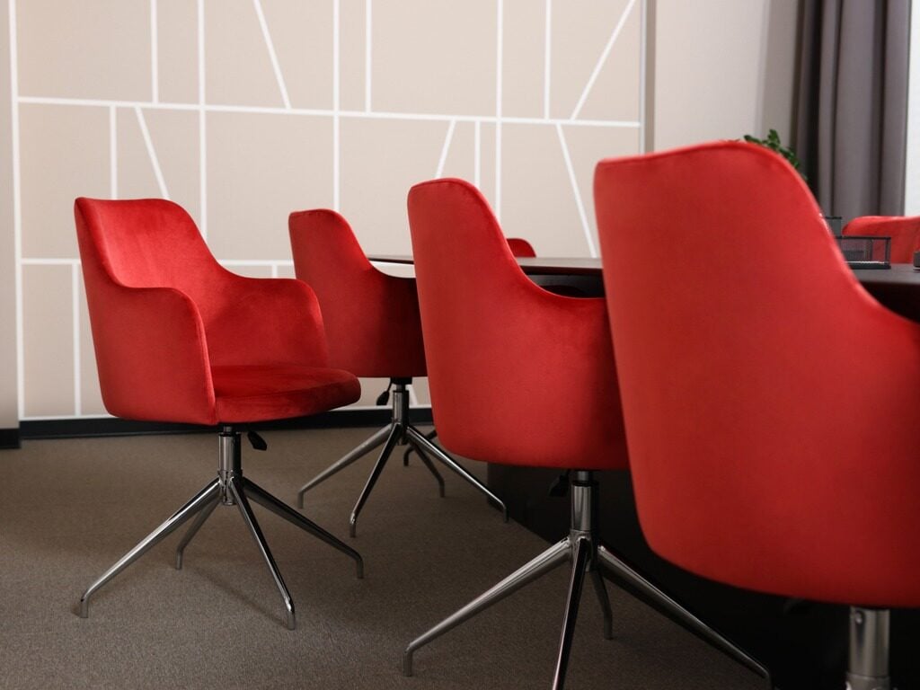 Red velvet chairs with chrome bases in a meeting room with a geometric wall pattern.